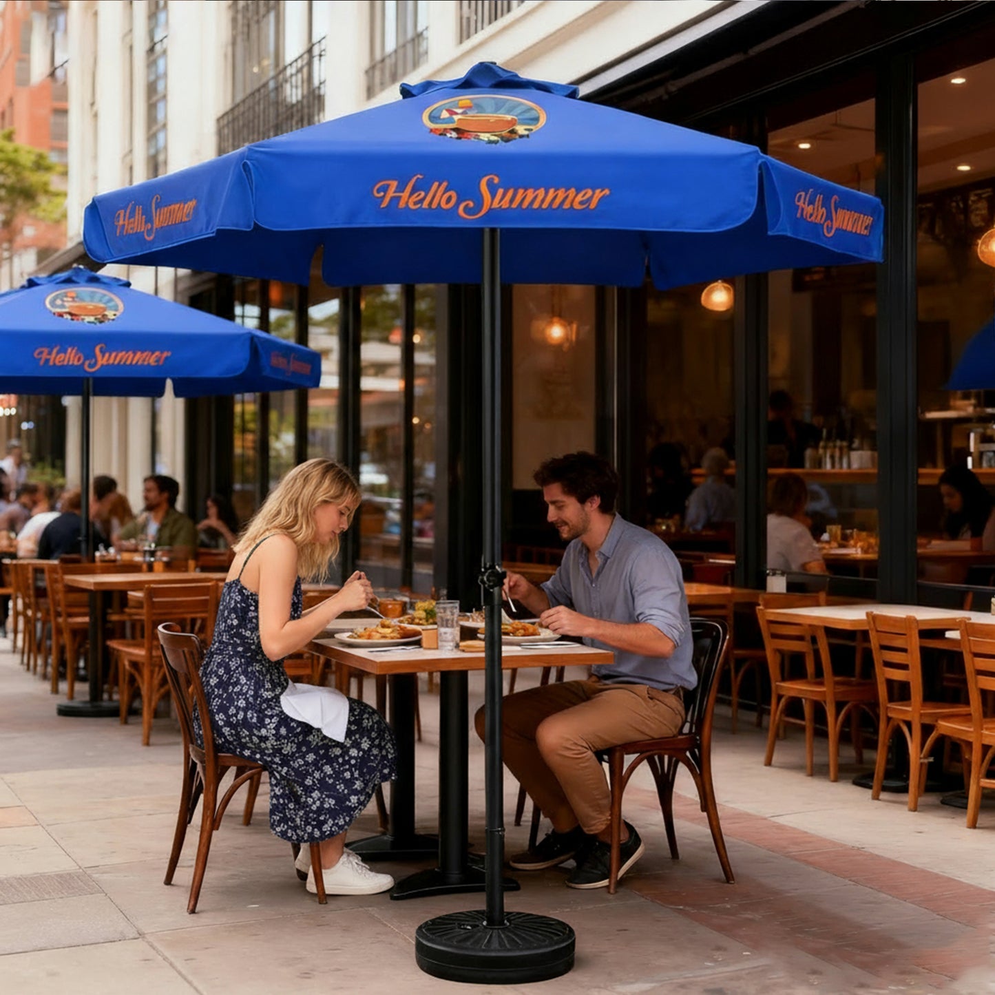 Two people dining under a blue 'Hello Summer' custom printed umbrella on a city street.